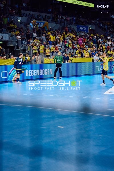 Ein Spieler der Rhein Neckar Löwen im gelben Trikot wirft den Ball ins Spiel ein, während ein Spieler von THW Kiel verteidigt.