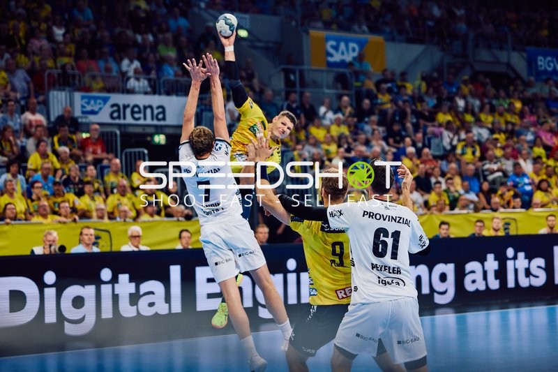 Ein Spieler der Rhein Neckar Löwen springt, um den Ball zu werfen, während zwei Spieler von THW Kiel versuchen, in der Abwehr zu blocken.