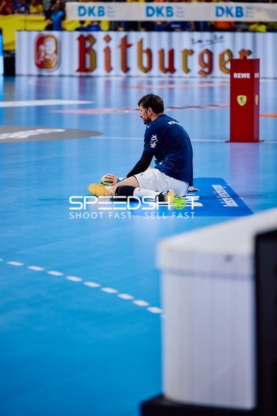 Ein Spieler sitzt auf dem Spielfeld und hält einen Handball in der Hand.