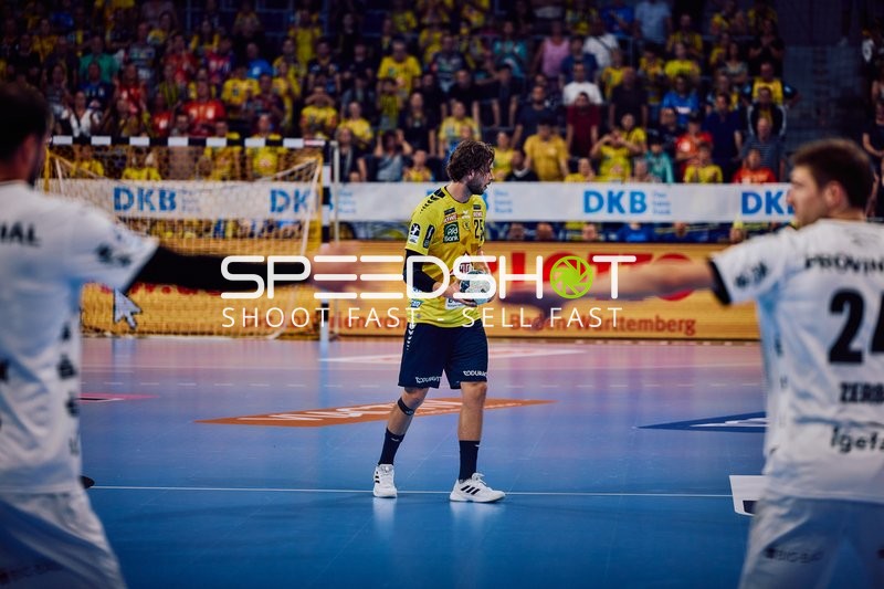 Ein Spieler von Rhein Neckar Löwen mit der Nummer 3 hält den Ball in der Mitte des Spielfelds, während Spieler von THW Kiel versuchen, ihn zu blockieren.