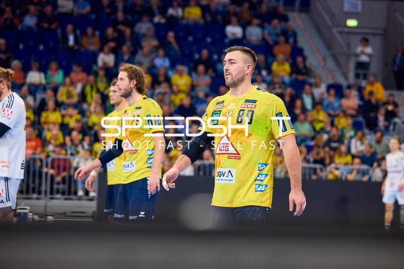 Spieler von Rhein Neckar Löwen stehen auf dem Spielfeld und schauen in Richtung des Spiels.