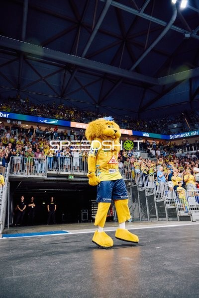 Das Maskottchen der Rhein Neckar Löwen steht vor einer vollen Zuschauermenge in der Arena.