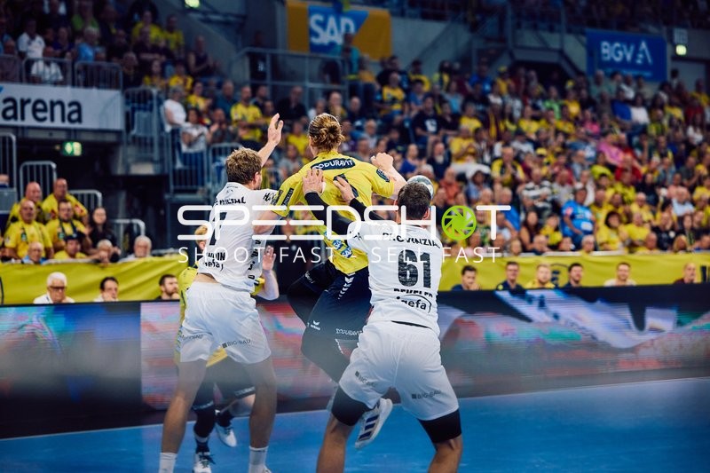 Ein Spieler der Rhein Neckar Löwen springt für einen Wurf, während zwei Spieler von THW Kiel verteidigen.