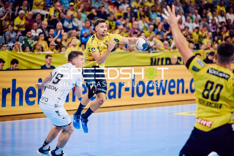 Ein Spieler von Rhein Neckar Löwen im gelben Trikot springt zum Wurf, während ein Spieler von MT Melsungen versucht zu verteidigen.