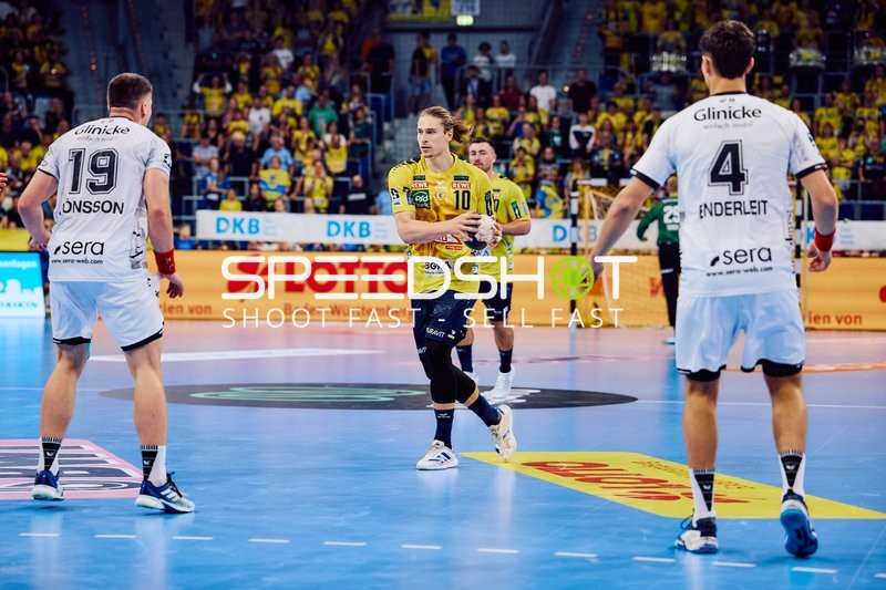 Ein Spieler von Rhein Neckar Löwen bereitet sich darauf vor, den Ball zu passen, während zwei Spieler von MT Melsungen ihn verteidigen.