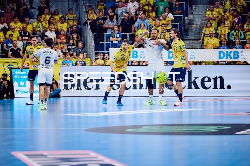 Ein Spieler von MT Melsungen in weißem Trikot mit der Nummer 6 ist im Zweikampf mit einem Spieler von Rhein Neckar Löwen in gelbem Trikot auf der Spielfläche.