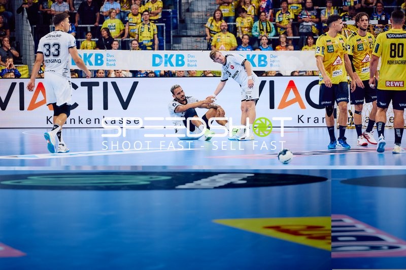 Ein Spieler von MT Melsungen sitzt auf dem Boden, während ein anderer ihm aufhilft. Spieler von Rhein Neckar Löwen stehen daneben.