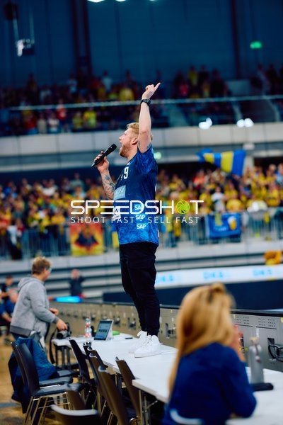 Ein Moderator mit Mikrofon spricht zu den Zuschauern.