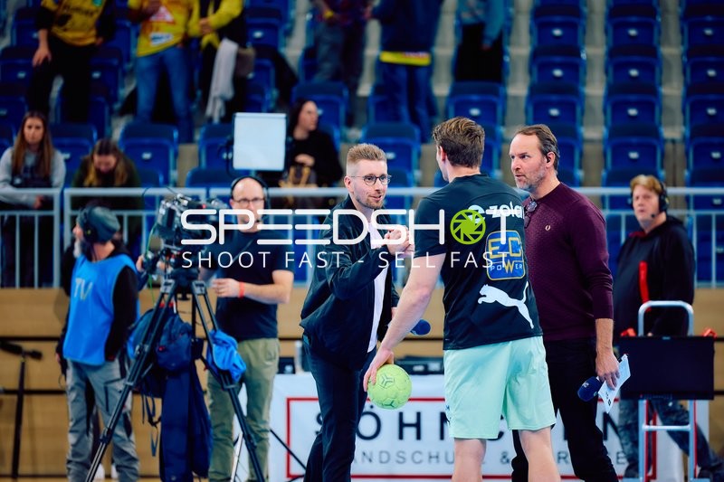 Interaktion zwischen einem Handballspieler und TV-Personal am Spielfeldrand.