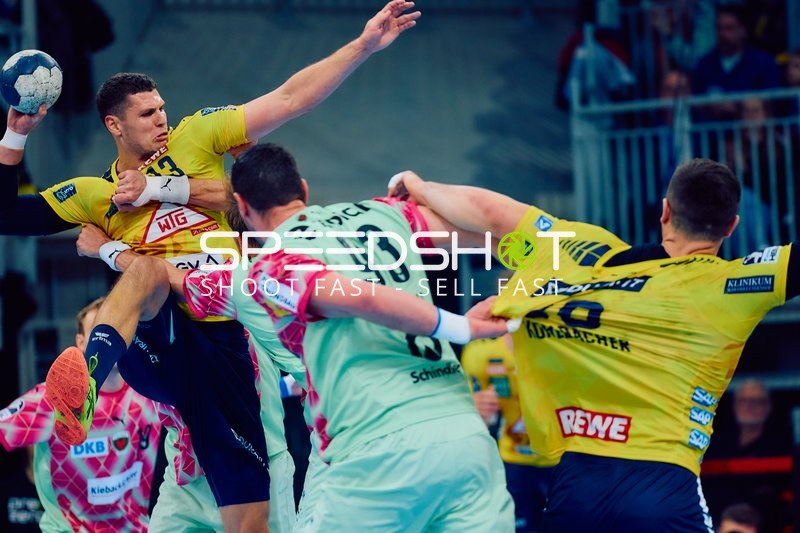 Ein Spieler der Rhein Neckar Löwen springt mit dem Ball in der Hand, während ein Spieler der Füchse Berlin versucht, ihn zu blocken.