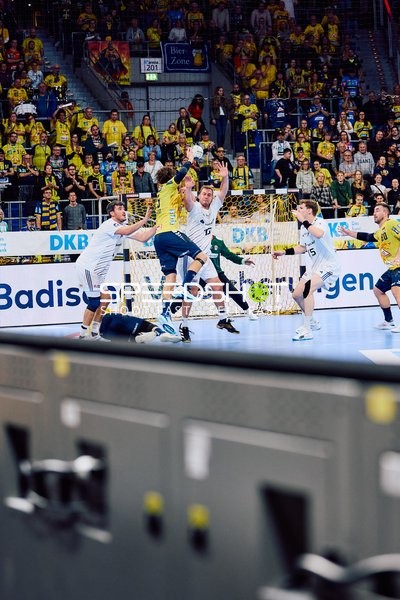 Ein Rhein Neckar Löwen-Spieler springt, um den Ball zu werfen, während mehrere HSV Hamburg-Verteidiger versuchen, den Wurf zu blockieren.