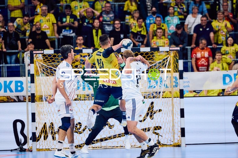 Ein Spieler der Rhein Neckar Löwen im gelben Trikot wirft den Ball Richtung Tor, während ein Spieler der HSV Hamburg in der Verteidigung aktiv ist.
