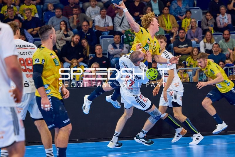 Ein Spieler der Rhein Neckar Löwen mit der Nummer 23 springt kraftvoll zum Torwurf, während er von einem Gegenspieler mit der Nummer 7 des HC Erlangen verteidigt wird.