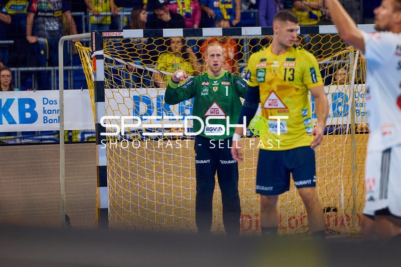 Ein Spieler der Rhein Neckar Löwen in gelbem Trikot hebt die Arme vor dem Tor, während der Torhüter verteidigt.