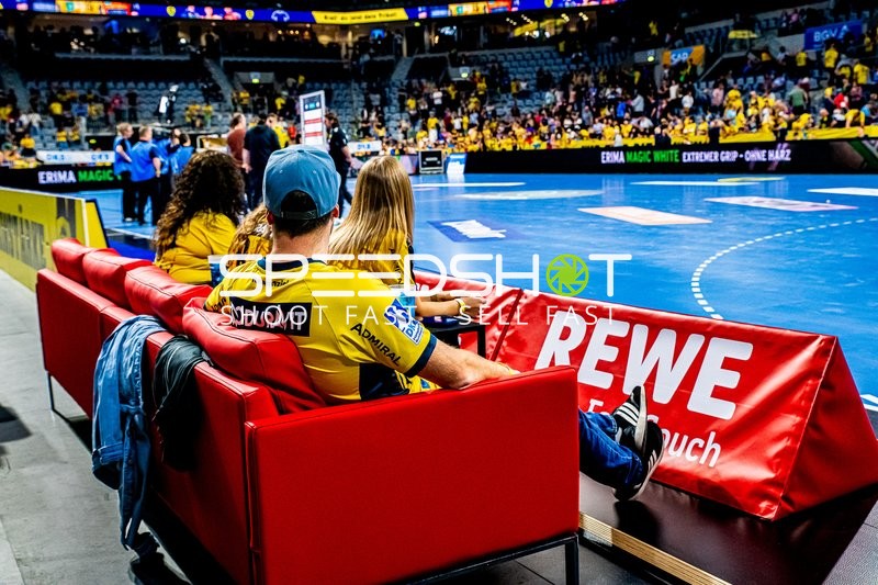 Zuschauer auf einer Couch am Spielfeldrand während eines Handballspiels