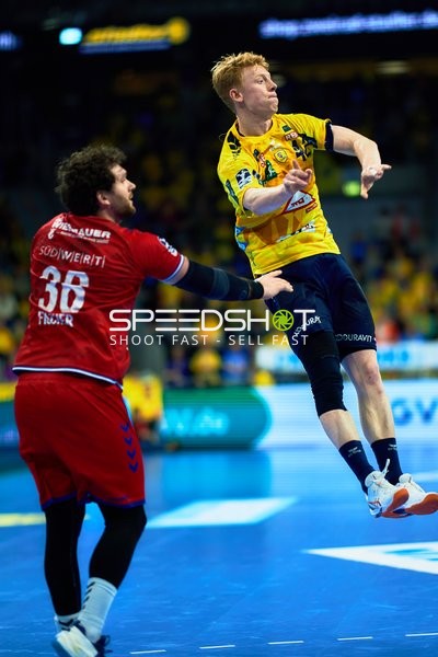 Ein Spieler der Rhein Neckar Löwen im gelben Trikot springt in die Luft, während ein Spieler von SG BBM Bietigheim versucht, ihn zu blocken.