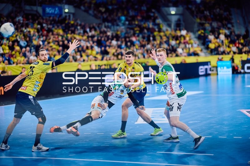 Ein Spieler von FRISCH AUF! Göppingen versucht einen Wurf, während zwei Spieler der Rhein-Neckar Löwen ihn verteidigen.