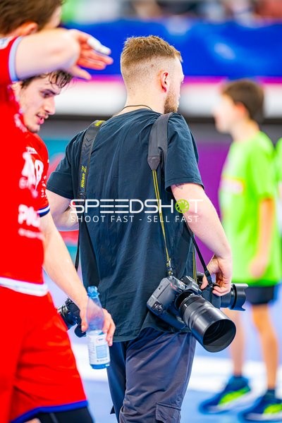Ein Fotograf bewegt sich auf dem Spielfeld, während Spieler im Hintergrund zu sehen sind.