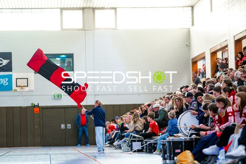 Ein Fan schwenkt eine rot-schwarze Fahne vor einer gefüllten Zuschauertribüne in der Halle.