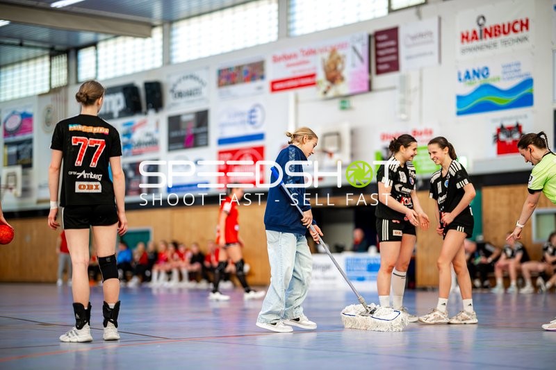 Ein Helfer wischt den Hallenboden, während Spieler auf dem Spielfeld stehen.