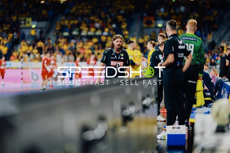 Das Bild zeigt Personen am Spielfeldrand, während ein Spiel stattfindet.