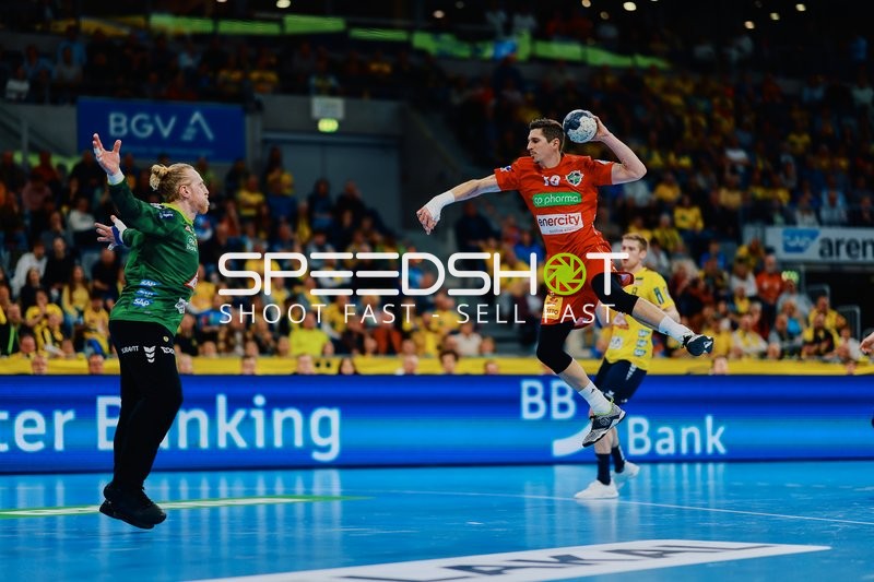 Ein Spieler von TSV Hannover Burgdorf springt in Richtung Tor für einen Wurf, mit einem gegnerischen Torwart im Vordergrund.