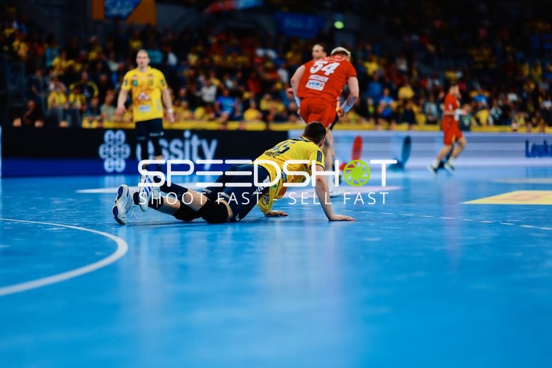 Ein Spieler der Rhein-Neckar Löwen liegt auf dem Boden, während ein Spieler der TSV Hannover Burgdorf im Hintergrund läuft.