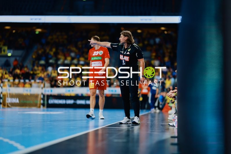 Ein Spieler von TSV Hannover Burgdorf steht auf dem Spielfeld, während eine Person an der Seitenlinie Anweisungen gibt.