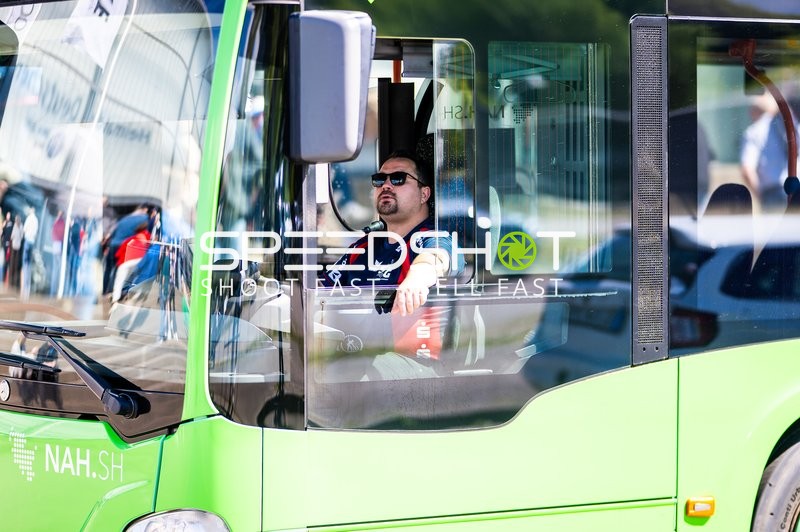 Ein Mann sitzt im Fahrerhaus eines grünen Busses mit Sonnenbrille und trägt ein Flensburg Trikot
