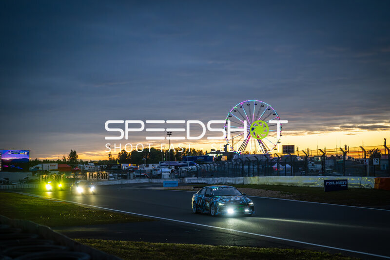 Rennfahrzeuge im Sonnenuntergang am Nürburgring mit leuchtendem Riesenrad