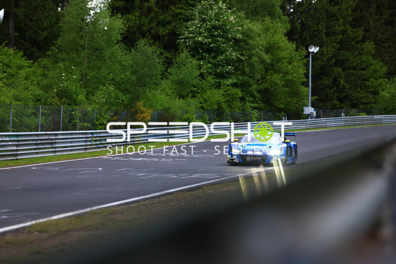 Blauer Rennwagen mit eingeschalteten Scheinwerfern auf der Nordschleife