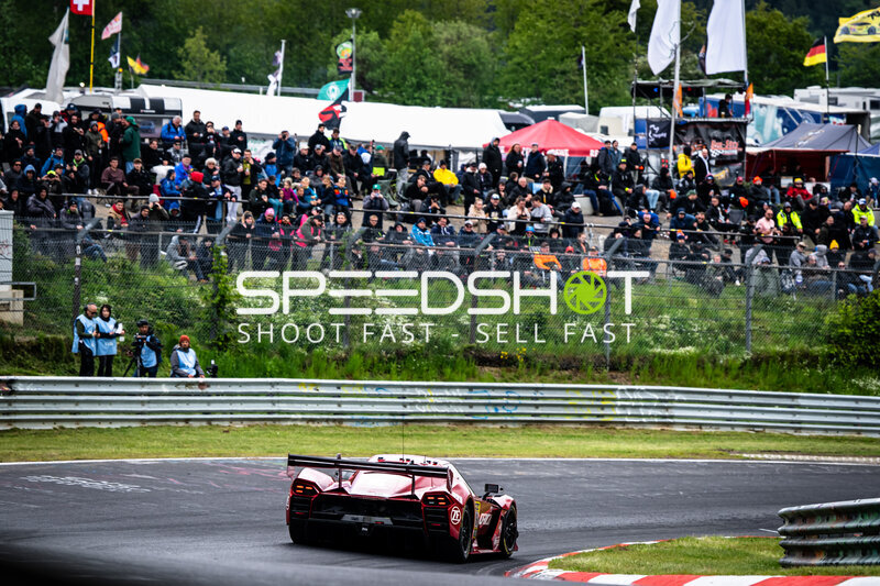 Roter Rennwagen durchfährt Kurve vor vollem Zuschauerbereich am Nürburgring