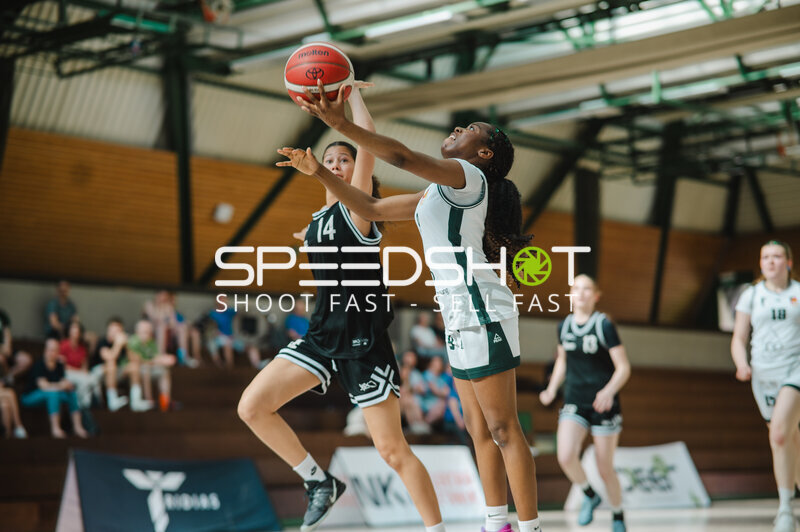 Spielerin (#9; Weiß-Grün) wirft Basketball über Defensivspielerin (#14; Schwarz)