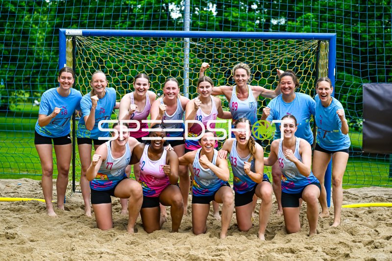 Frauenmannschaft posiert jubelnd vor dem Beachhandball-Tor