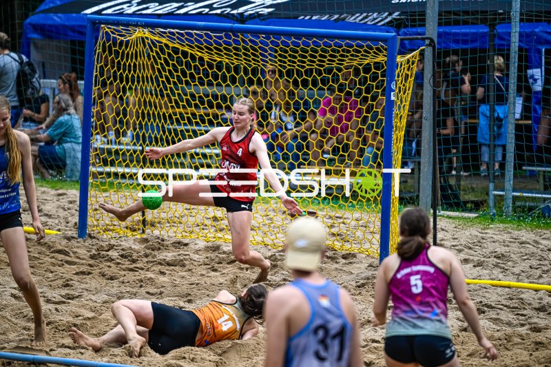 Torfrau (#4; rot) pariert mit dem Fuß beim Beach-Handball