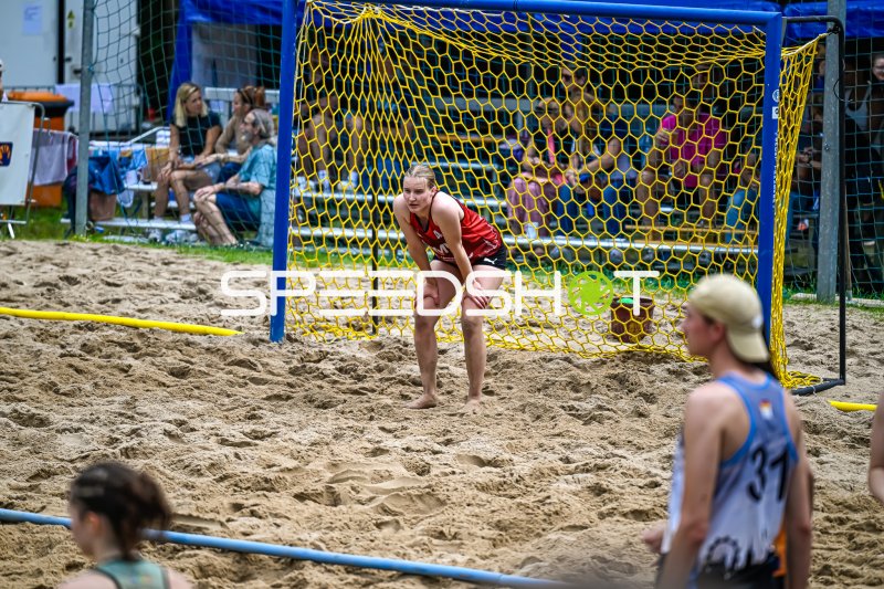 Torfrau im roten Trikot lauert vor dem Beachhandball-Tor