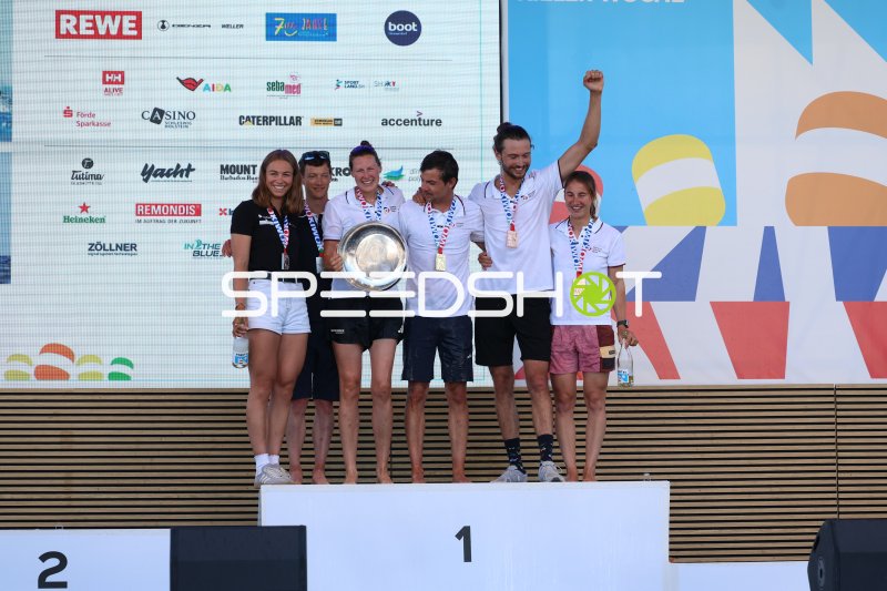 Siegerehrung Kieler Woche 2026: Segelteam mit Pokal auf Olympiazentrum-Podium